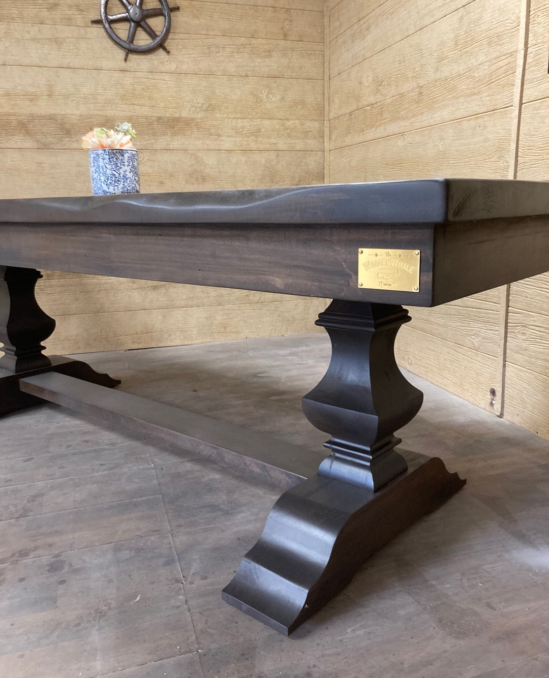 Close-up of a dark stained pedestal dining table with a brass maker's plate